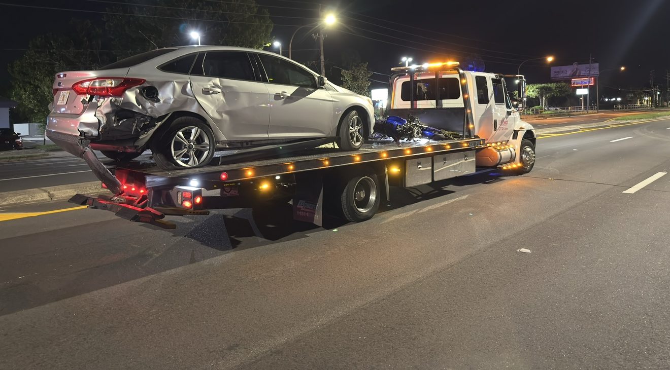 A damaged sedan being loaded onto a flatbed tow truck at night after a collision