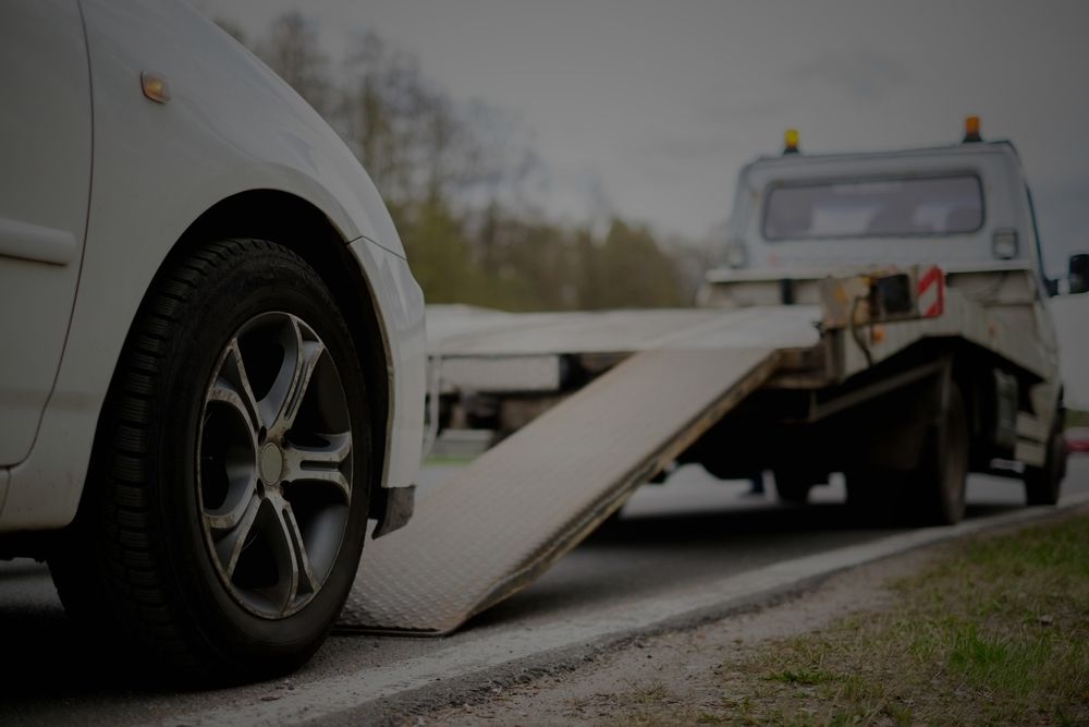 The front wheel of a car on the ramp of a flatbed tow truck